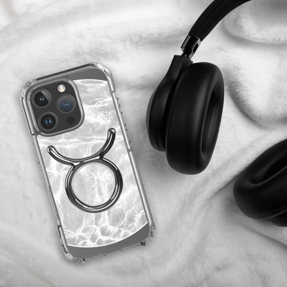 Zodiac Taurus MagSafe clear iPhone case with metallic design, laid beside black headphones on soft fabric.