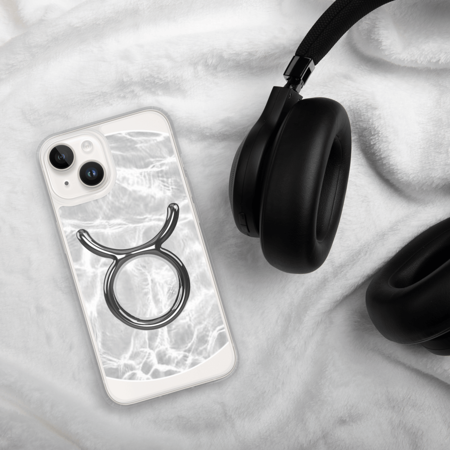 Zodiac Taurus Magsafe clear iPhone case with marble design beside black headphones on soft blanket.