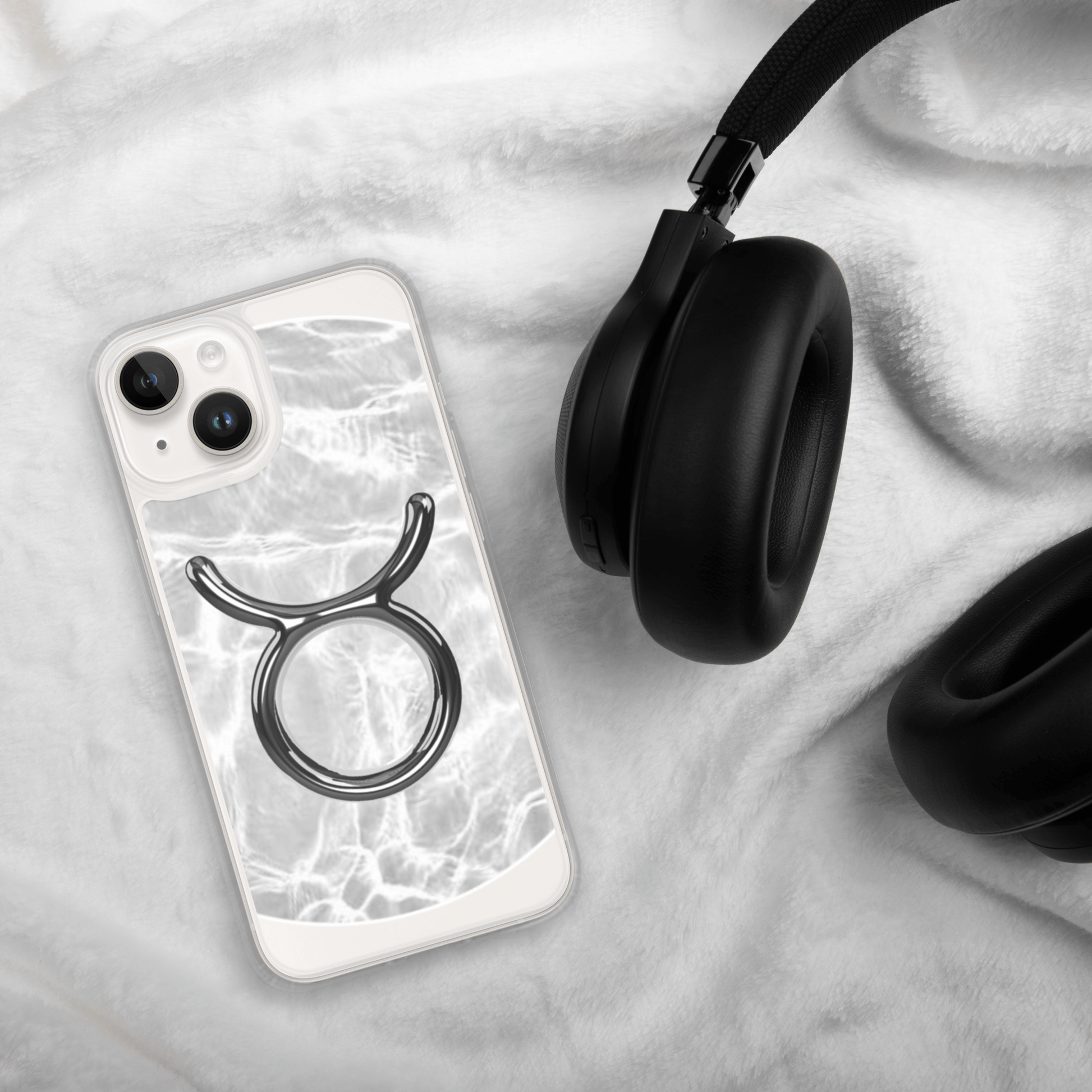 Zodiac Taurus Magsafe clear iPhone case with marble design beside black headphones on soft blanket.