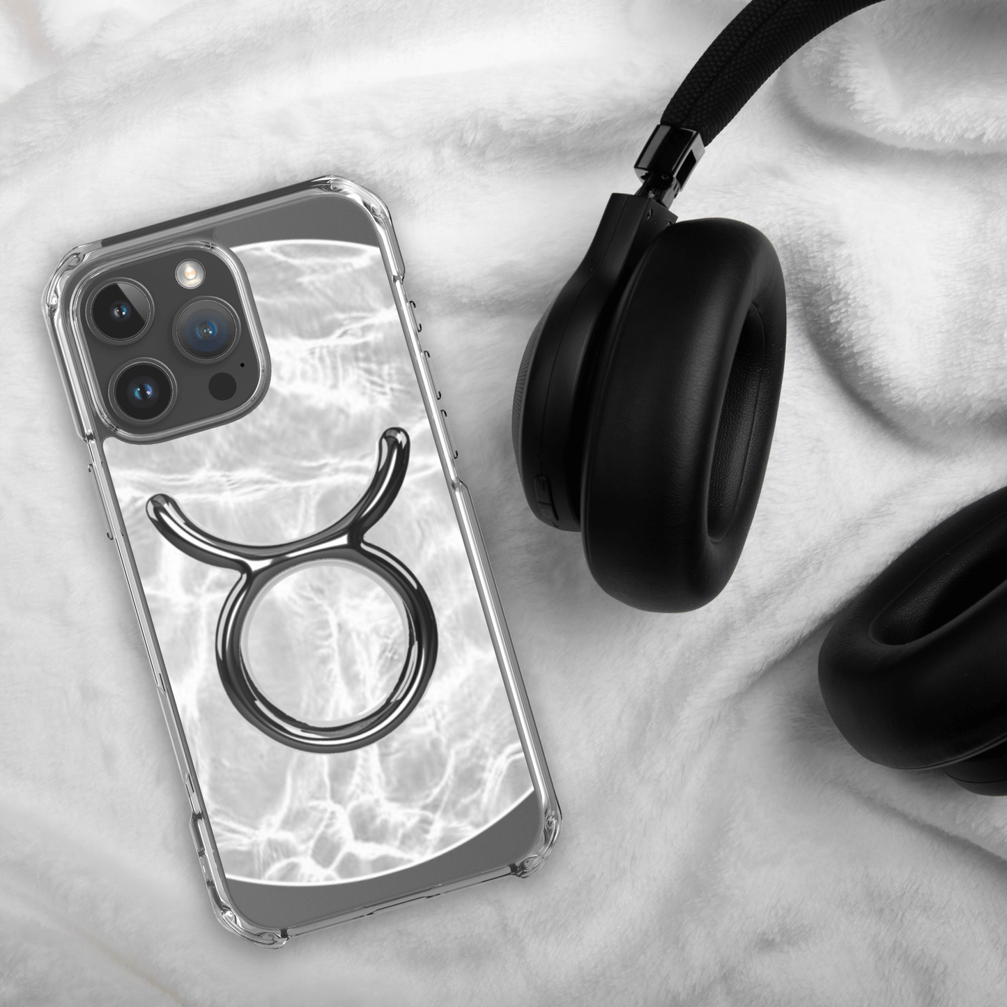 Zodiac Taurus Magsafe clear iPhone case with marble design, laid beside black headphones on soft fabric surface.