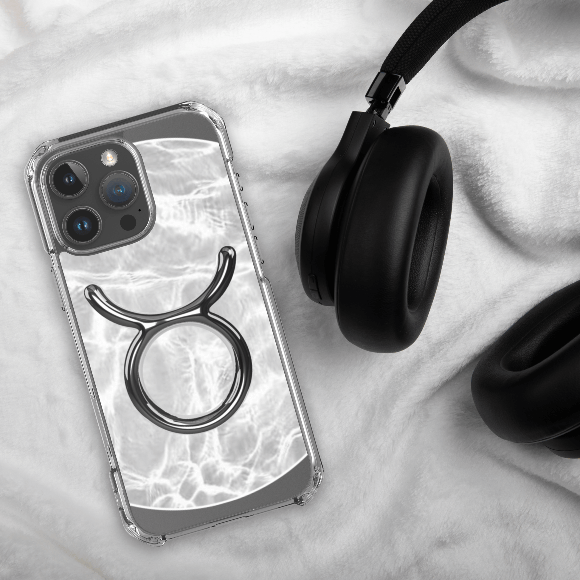 Zodiac Taurus Magsafe clear iPhone case with marble design, laid beside black headphones on soft fabric surface.