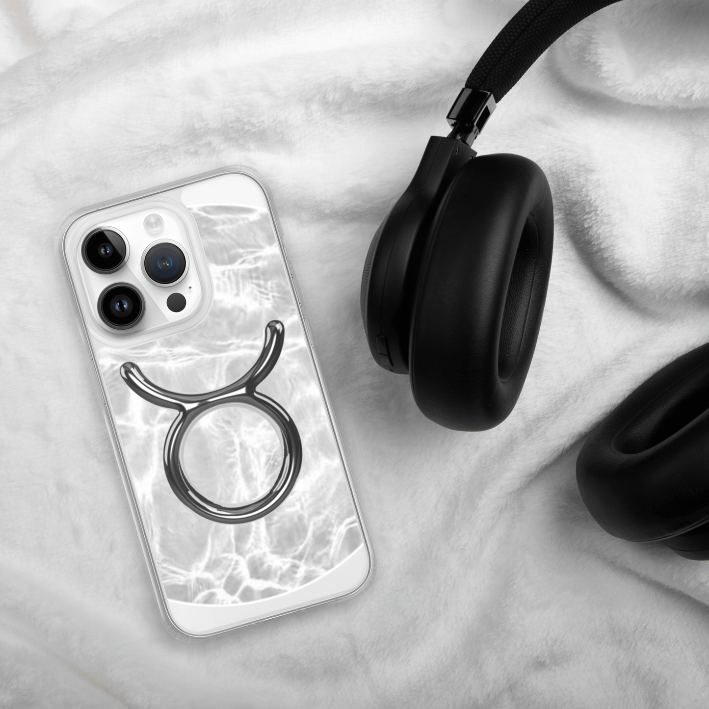 Zodiac Taurus Magsafe clear iPhone case with metallic design on a soft surface next to black headphones.