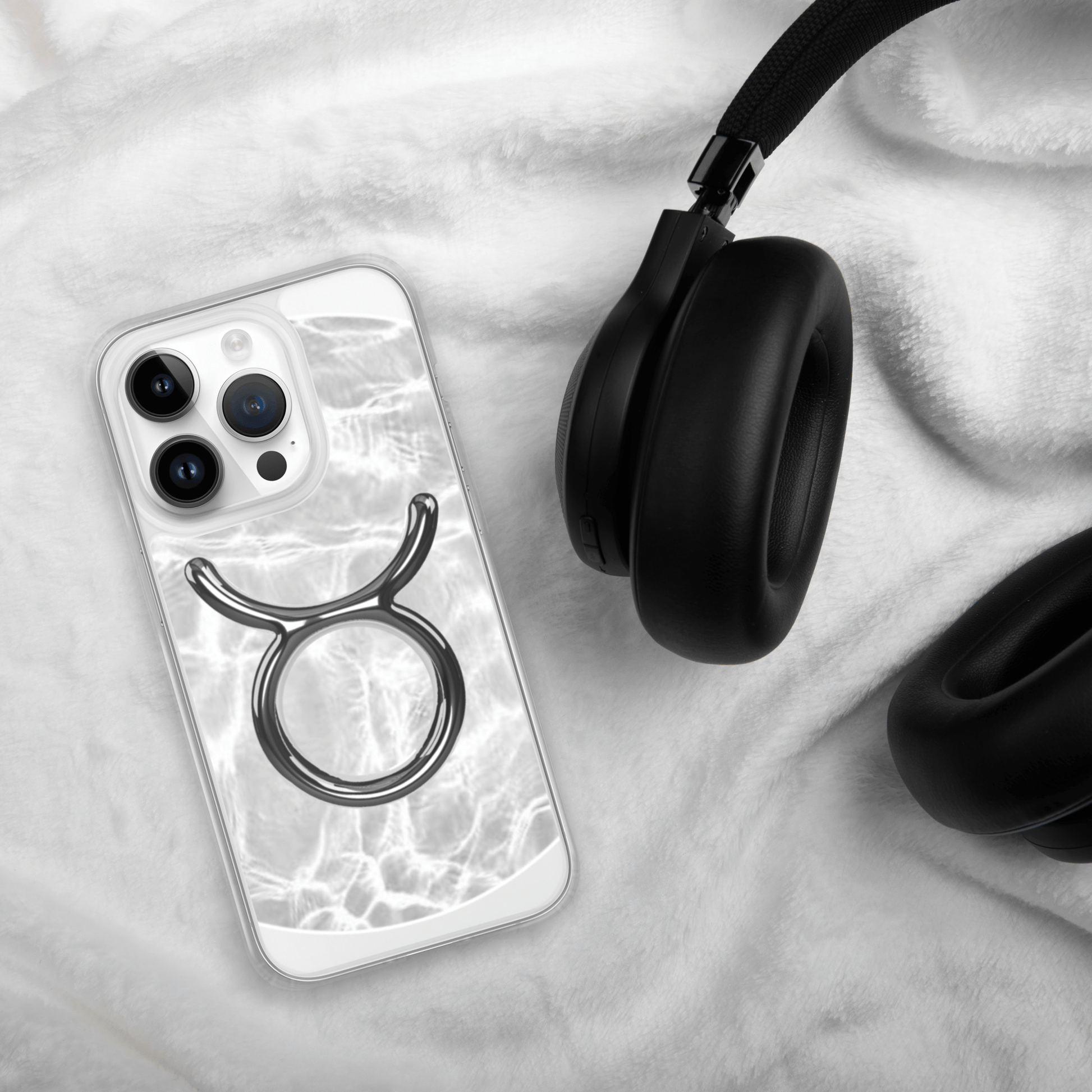 Zodiac Taurus Magsafe clear iPhone case with metallic design on a soft surface next to black headphones.